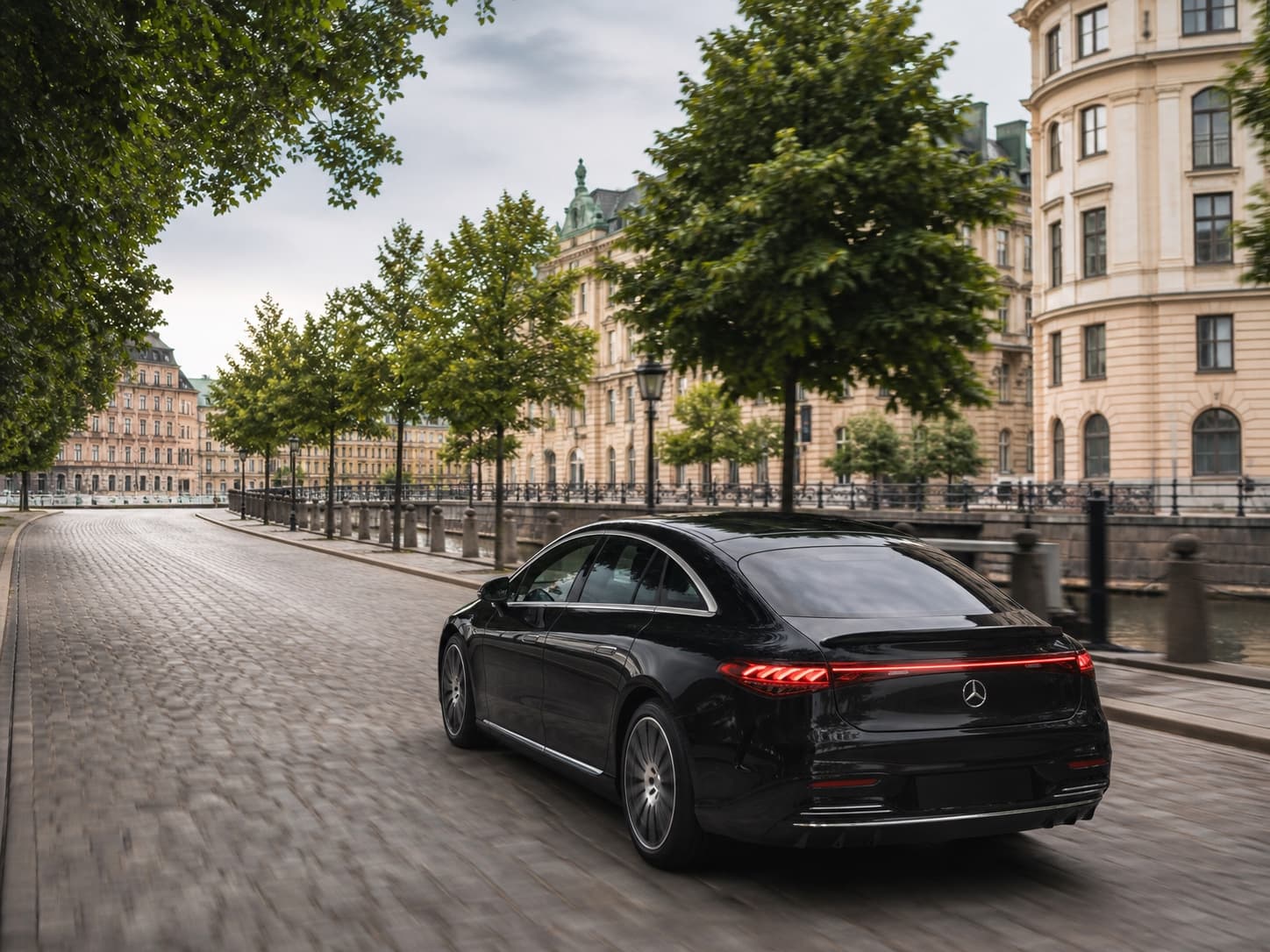 A chauffeur opening the door of a black Mercedes-Benz on a city street